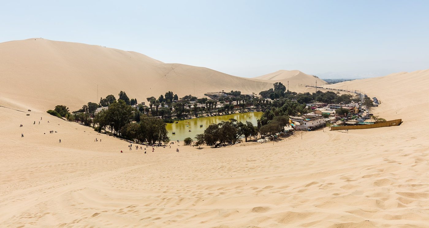 Huacachina oasis and its lagoon ringed by palms and giant sand dunes near Ica, Peru