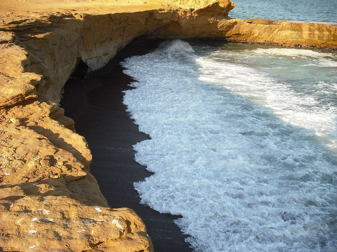 Surf washing over the dark red sand of Playa Roja in Paracas National Reserve