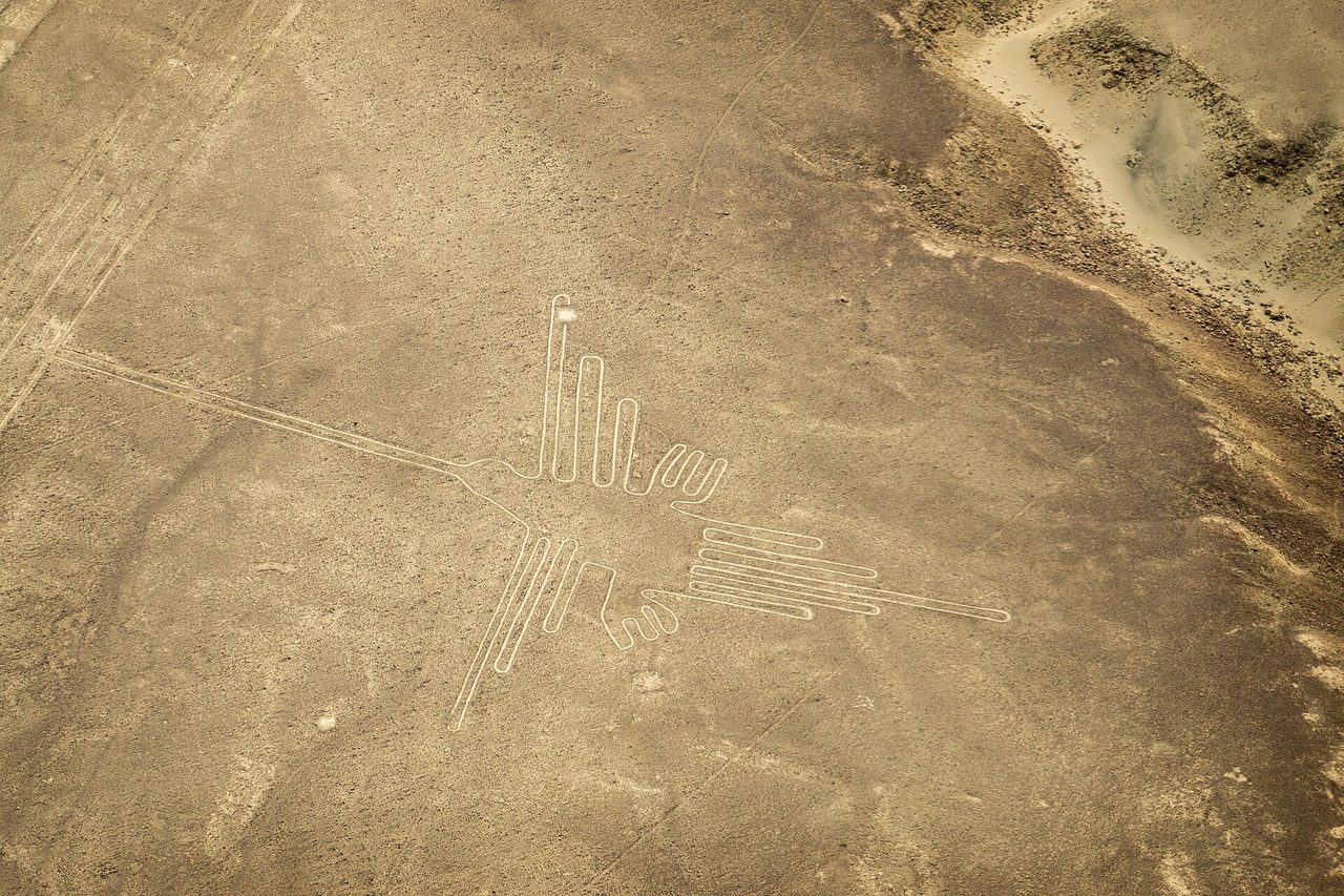 Aerial view of a large bird geoglyph scratched into the pale desert floor of the Nazca plain