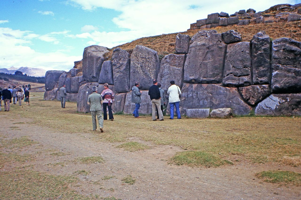 Visitors standing beside the massive interlocking megaliths of the Sacsayhuaman walls on the hillside above Cusco
