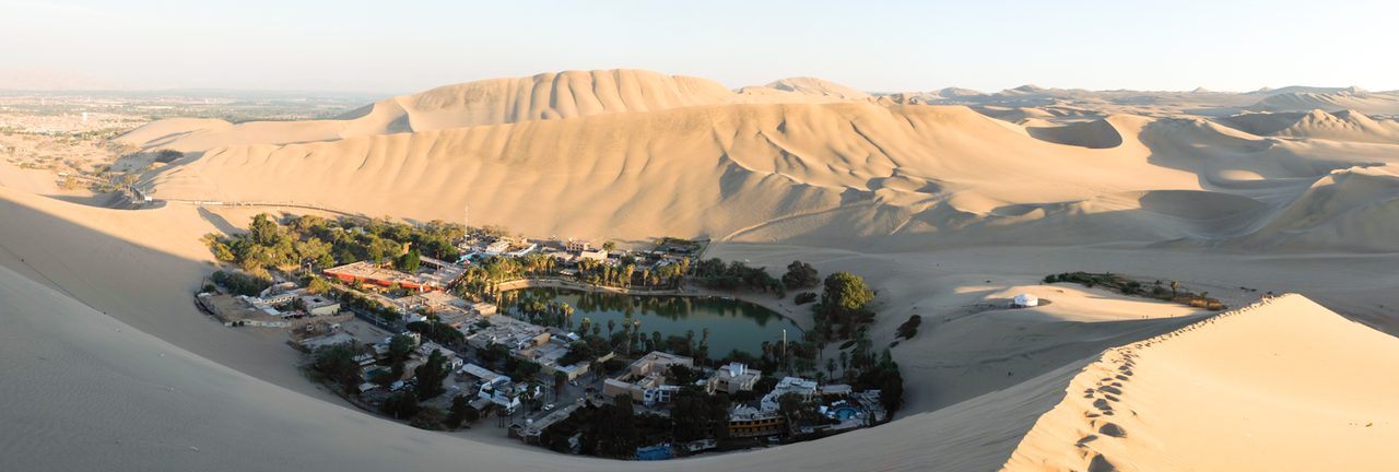 Sand dunes rising above the Huacachina oasis lagoon and its ring of palm trees near Ica on Peru’s southern coast