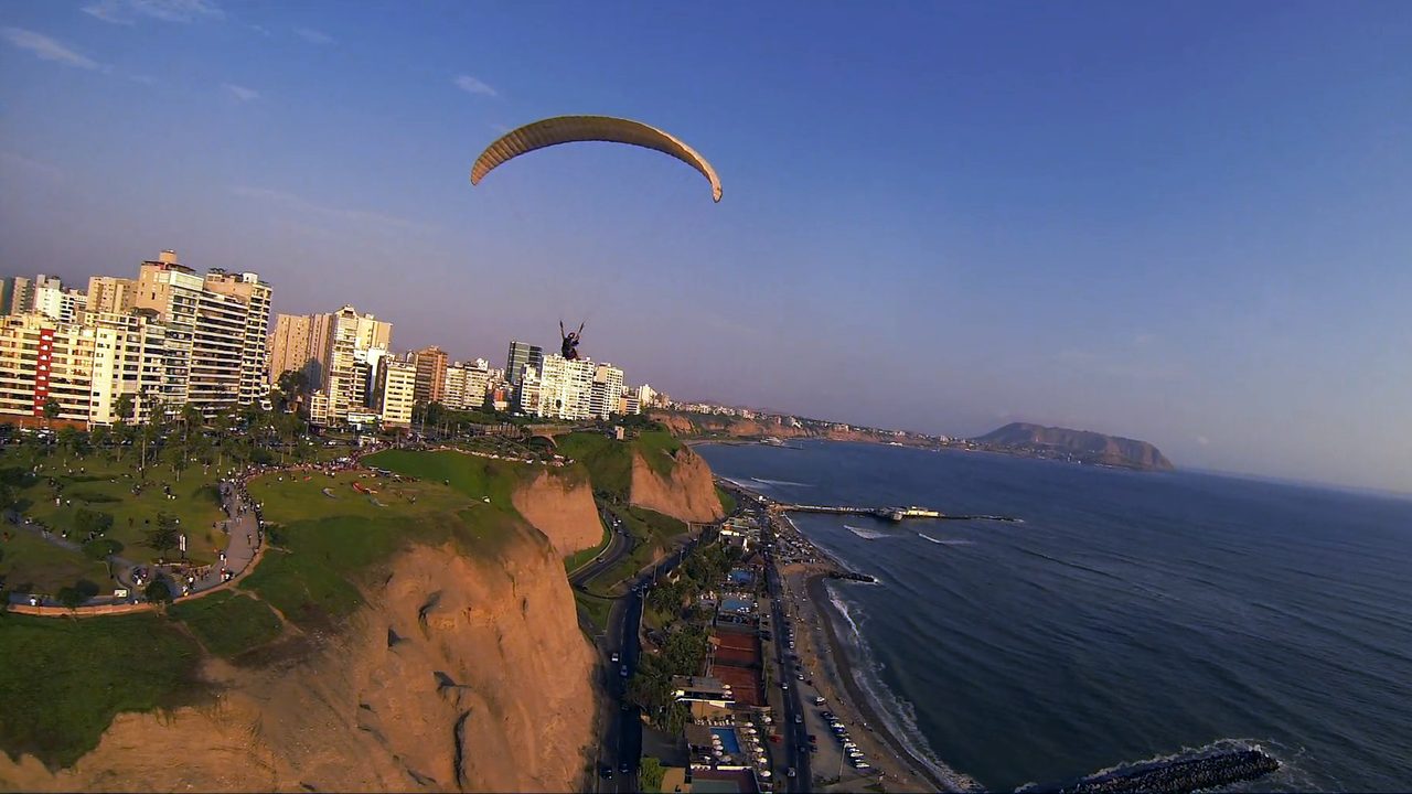 A tandem paraglider soaring over the Costa Verde cliffs and apartment blocks of Miraflores, Lima