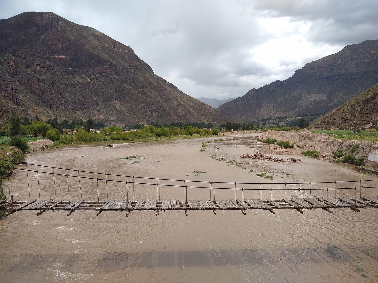 The Urubamba river running high and silty through the Sacred Valley at Lamay, with an old wooden footbridge across it