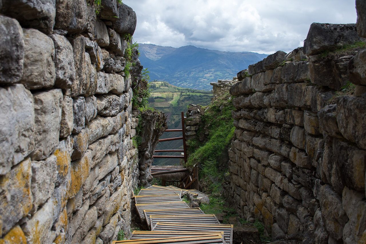 A narrow passage between the massive stone walls of the Kuelap fortress, looking out over the green Utcubamba valley
