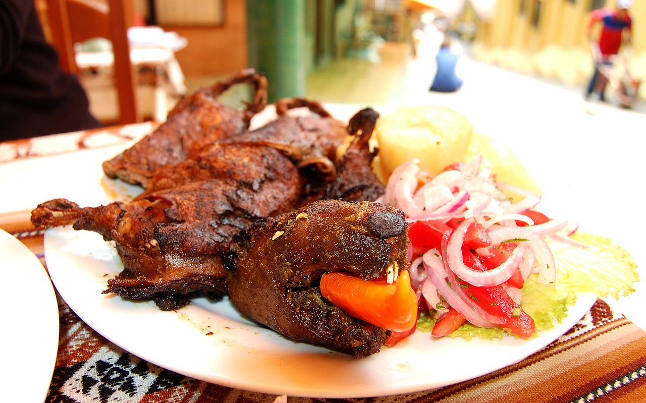 Cuy al horno served whole on the plate with potato and a salad of red onion and tomato