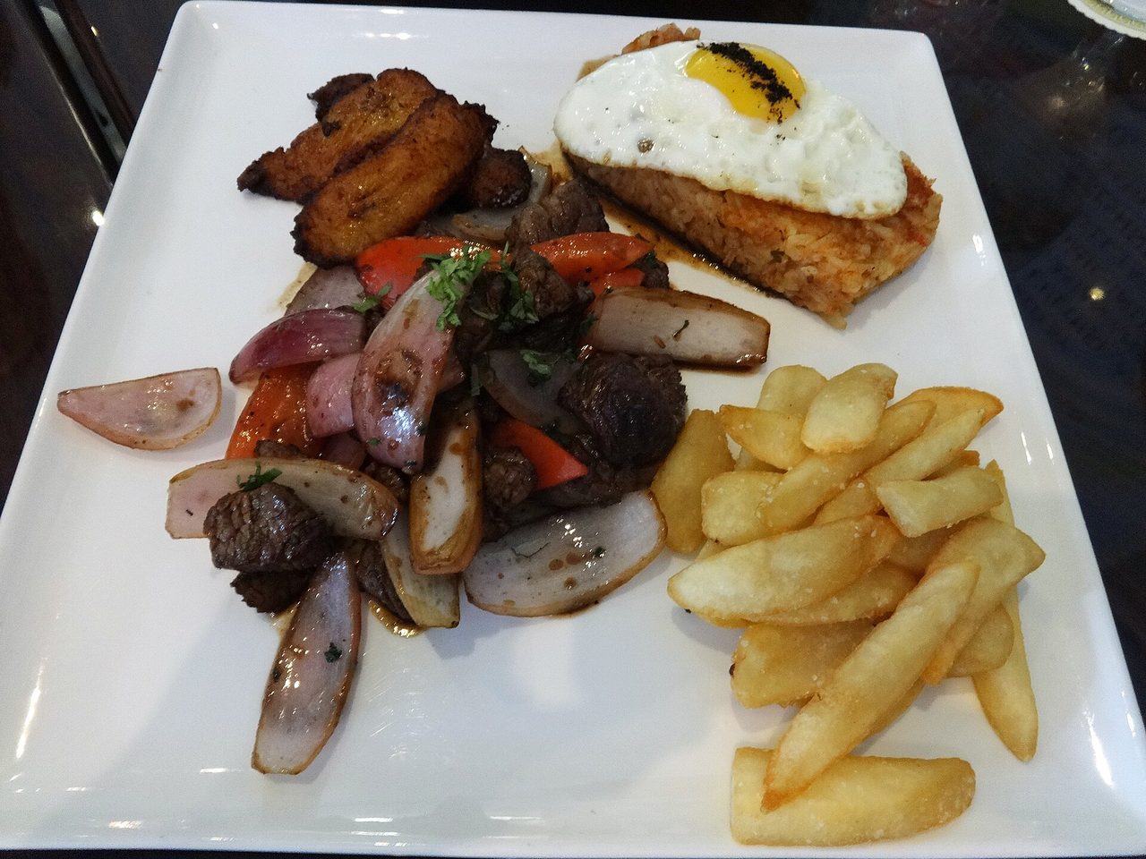 Lomo saltado a lo pobre: beef stir-fried with red onion and tomato, chips, fried plantain and a fried egg over tacu tacu