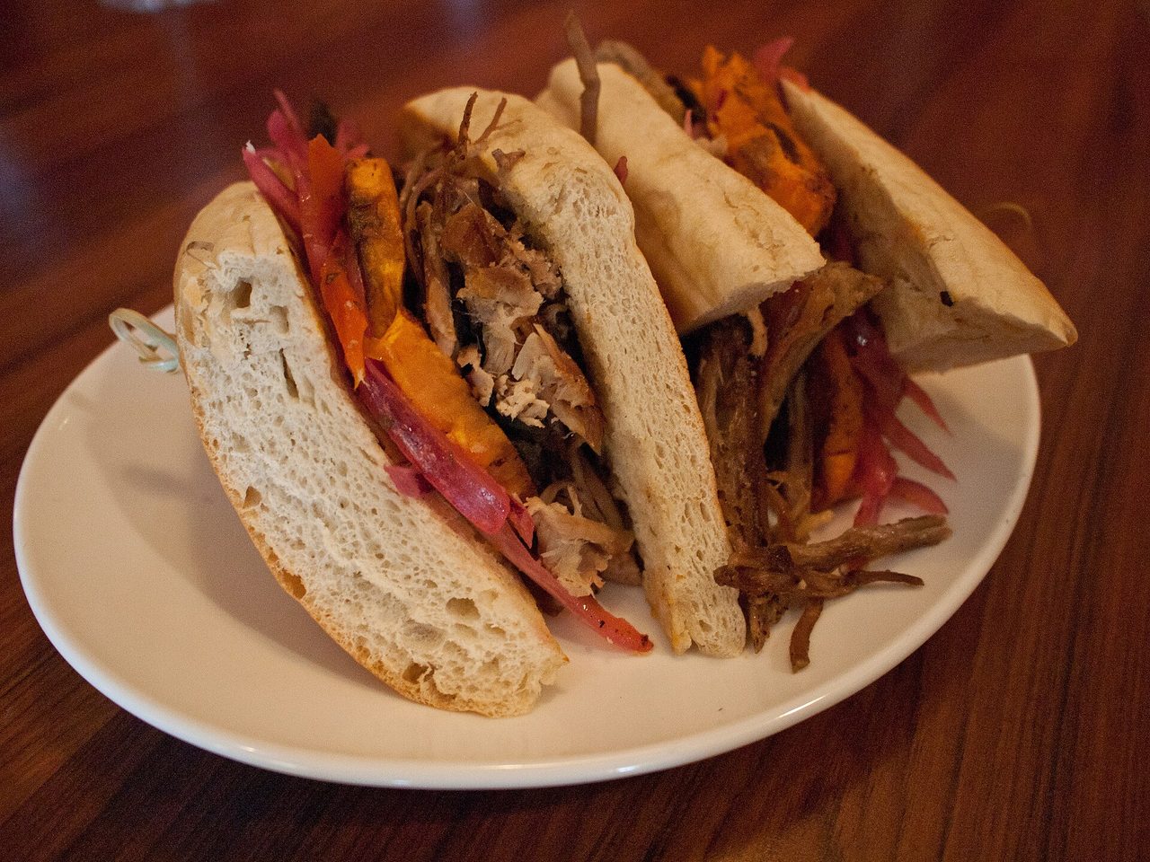 Two halves of a pan con chicharron sandwich on a white plate, filled with fried pork, sliced sweet potato and pickled red onion