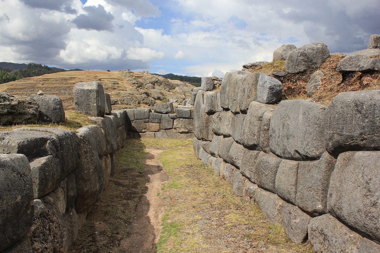 Massive fitted limestone blocks forming the zigzag ramparts of Sacsayhuaman above Cusco, with grassy terraces and Andean hills behind