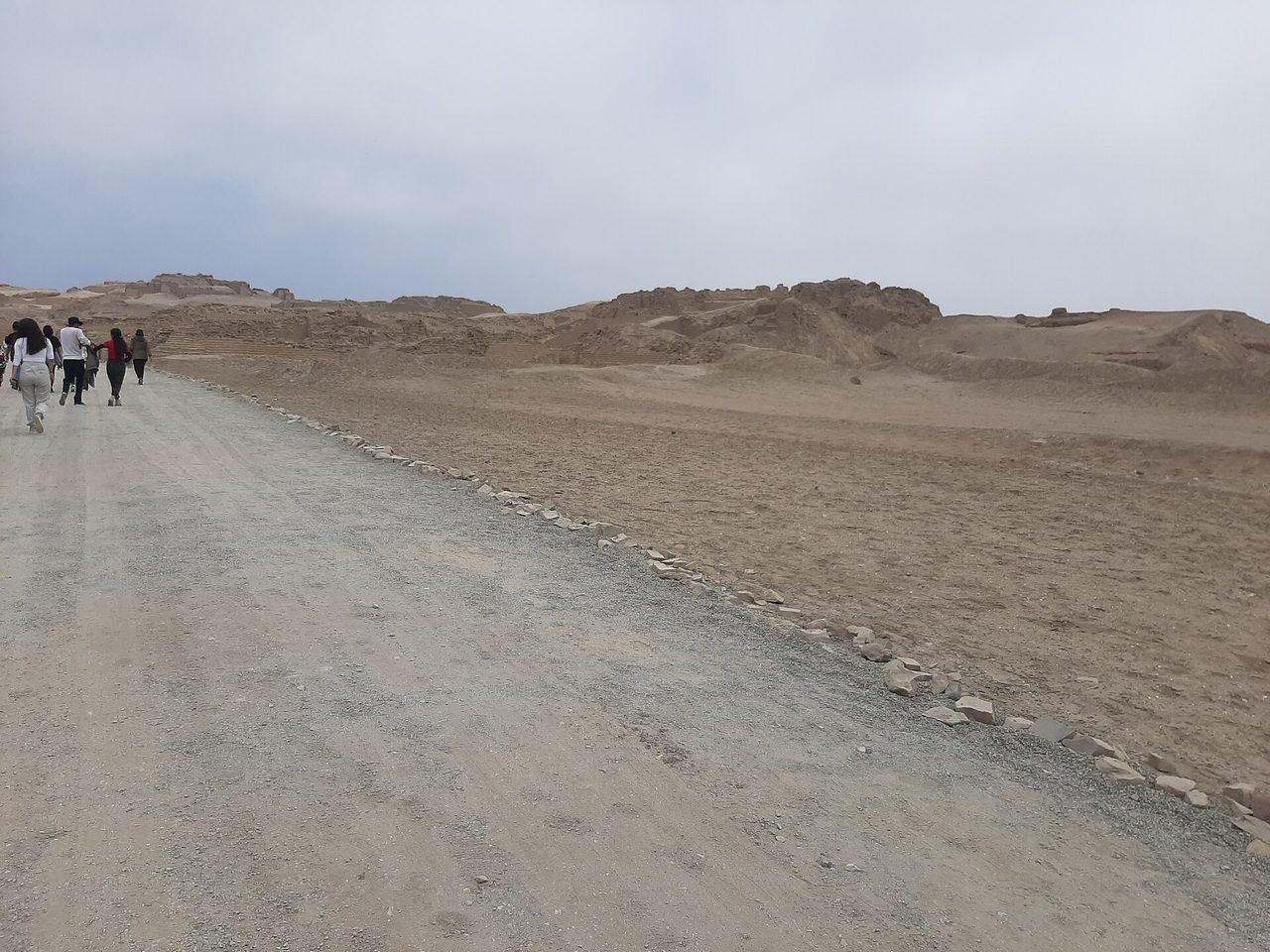 Visitors walking a dirt track through the sandy adobe ruins of the Pachacamac sanctuary south of Lima