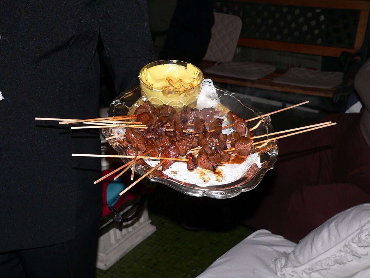 A platter of grilled anticucho skewers served with a glass of yellow chilli sauce