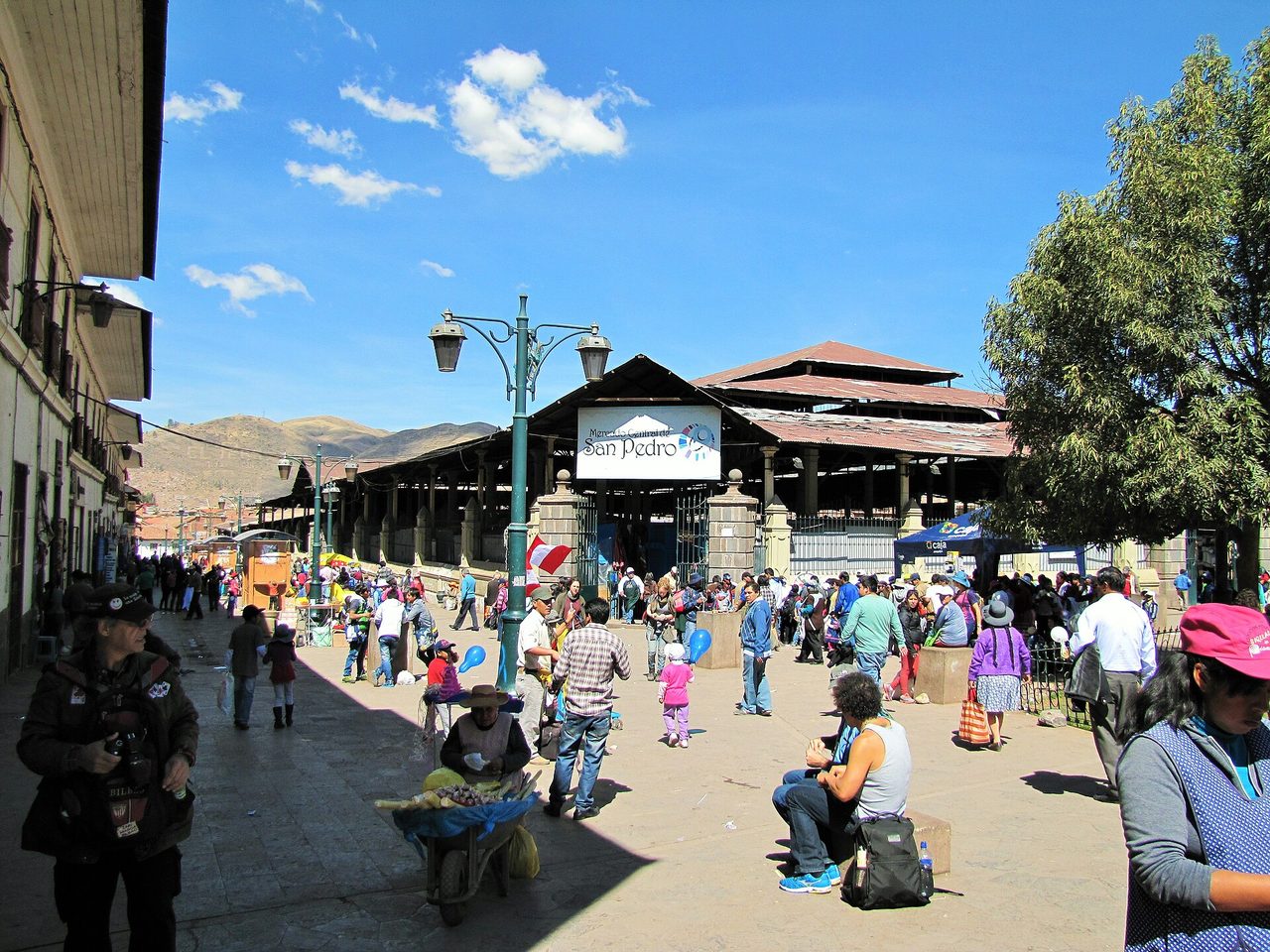 Crowds outside the entrance to Cusco's San Pedro central market, with a vendor pushing a barrow of produce in the foreground