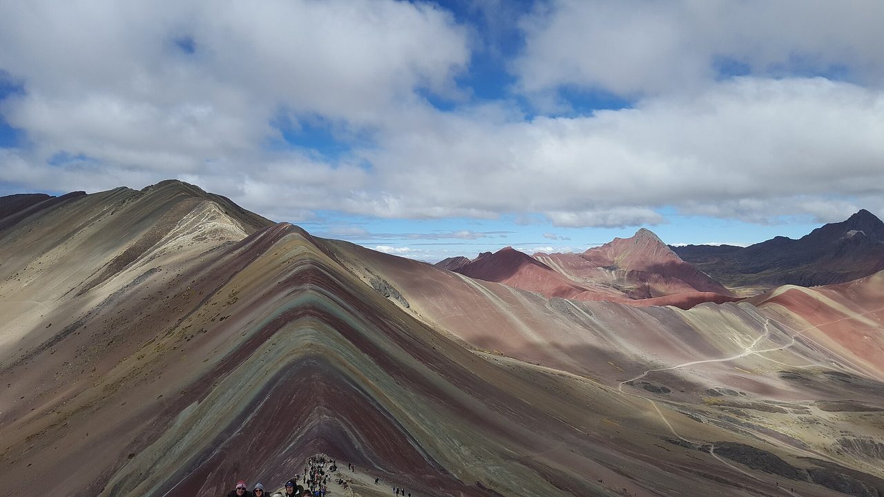 Visitors on the striped ridge of Vinicunca, the Rainbow Mountain, with the Red Valley behind