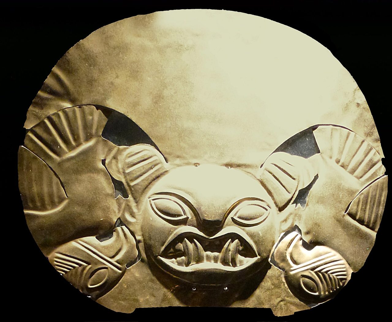 A Moche beaten-gold headdress ornament with a feline face, displayed against black in a Lima museum