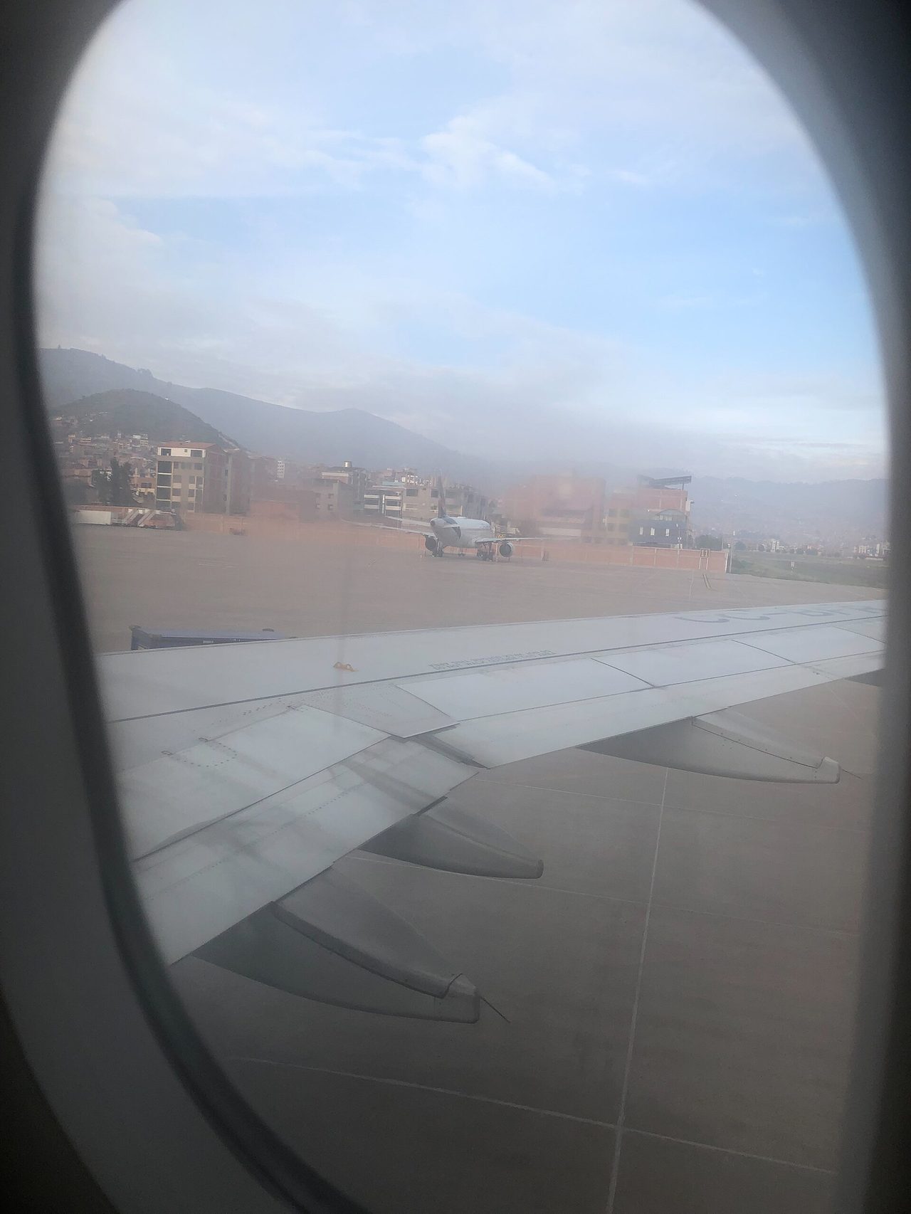 View from an aircraft window on the apron at Cusco airport, the city climbing the hills behind the runway
