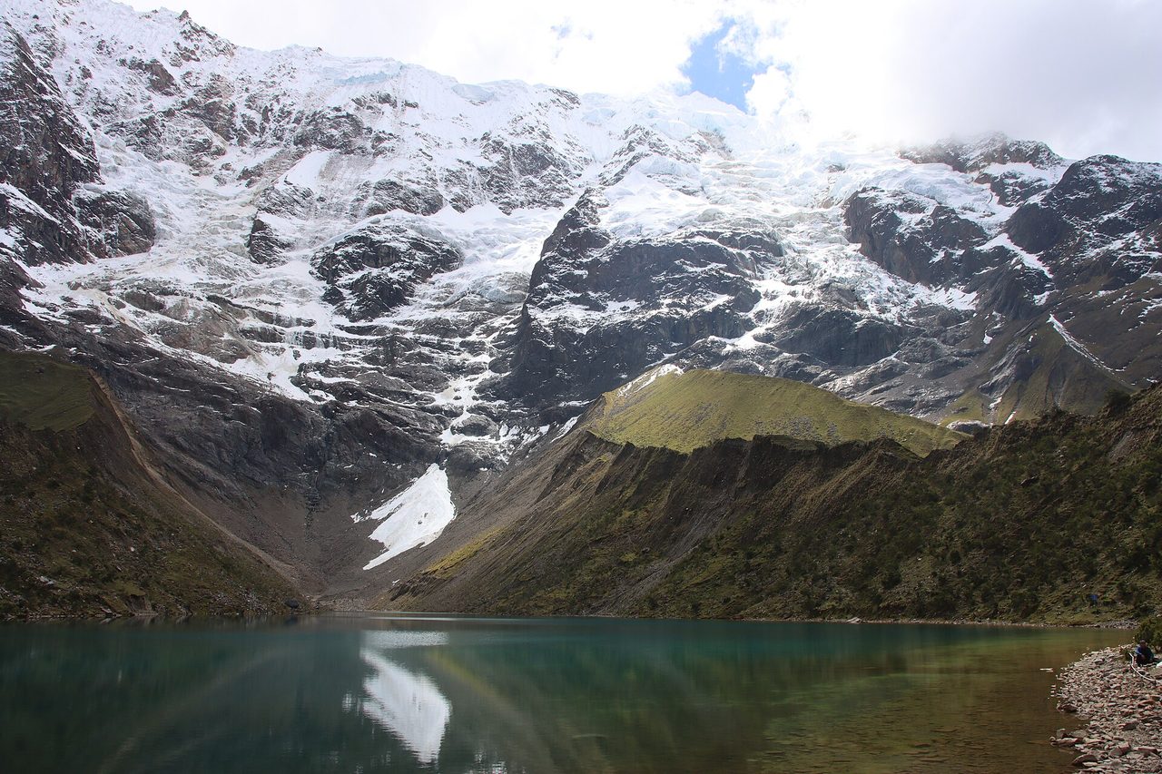 The stony near shore of Humantay Lake, with the moraine ridge on the right and hanging ice above the far end of the water