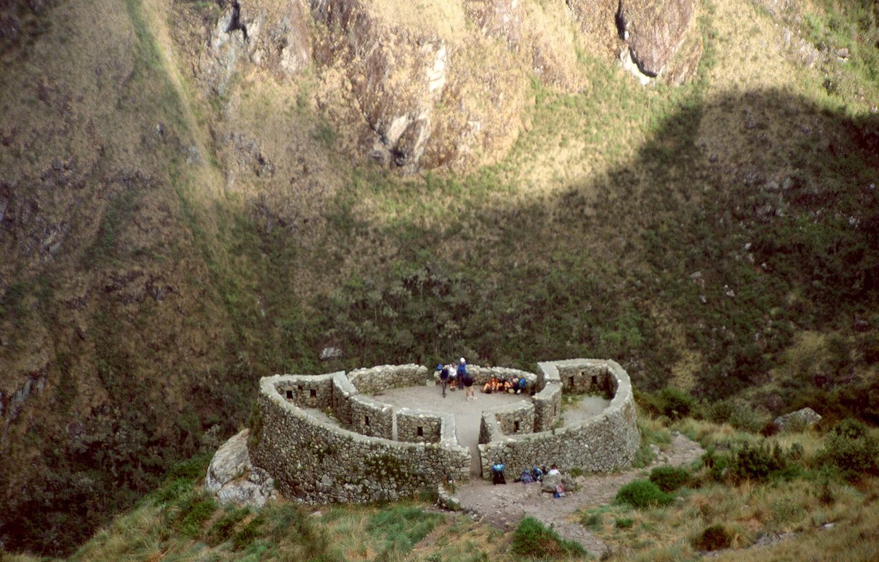 The oval stone walls of the Runkurakay tambo on the Inca Trail, with trekkers resting inside