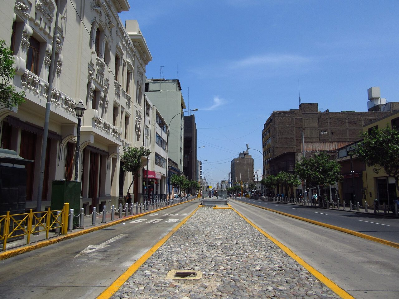 A wide avenue with a marked bus lane and a cobbled median in Cercado de Lima, republican-era buildings along one side