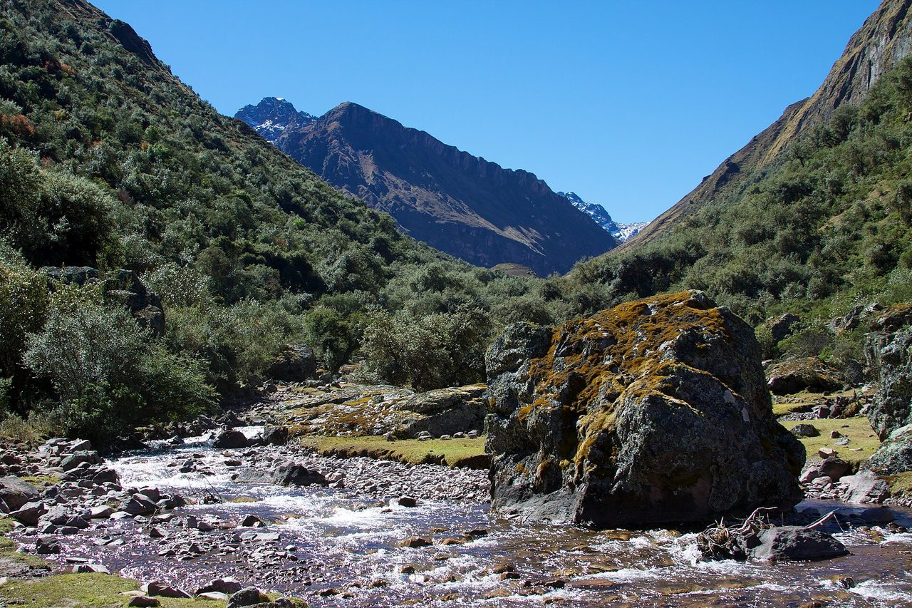 A clear stream running through the open valley above Huaran, one of the starting points for the Lares trek in the Cusco region of Peru, with snow-covered peaks at the head of the valley