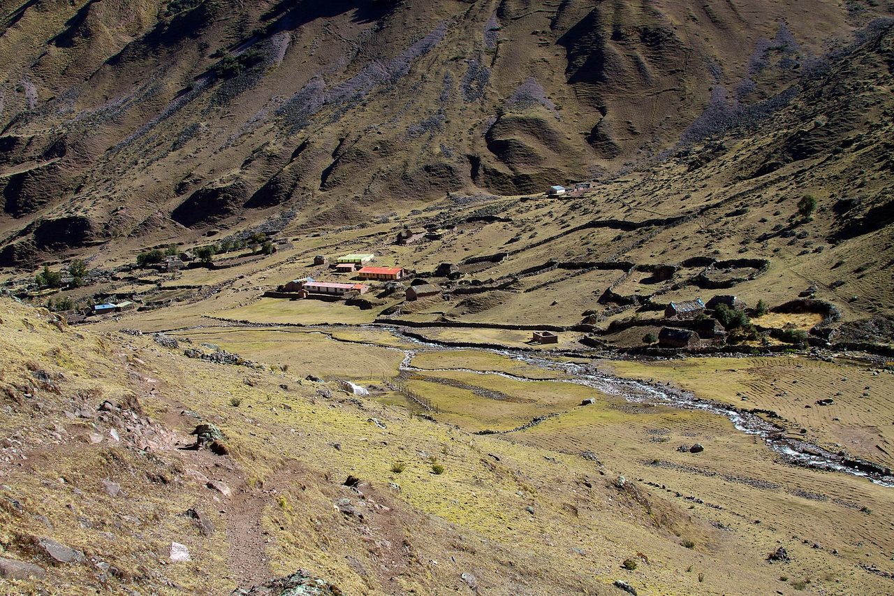 The Quechua settlement of Cancha Cancha seen from the trail above: a scatter of adobe and tin-roofed houses among stone-walled fields on a treeless hillside
