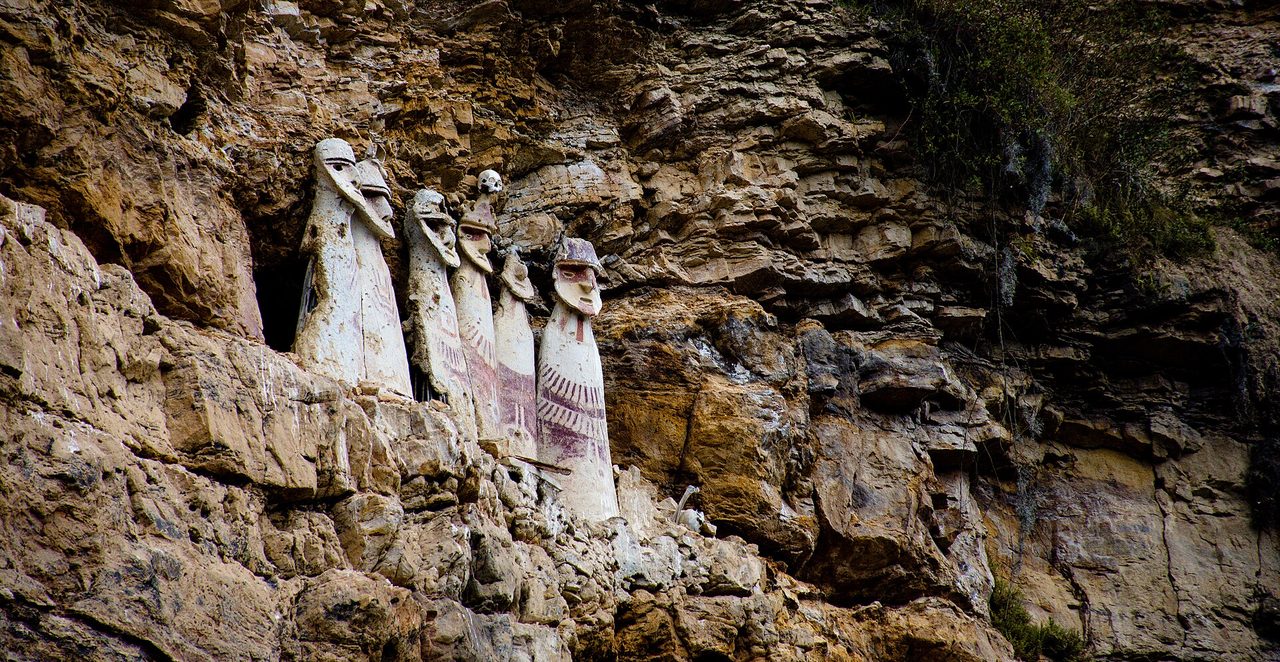 Six painted Chachapoya clay sarcophagi standing on a narrow cliff ledge at Karajia in northern Peru