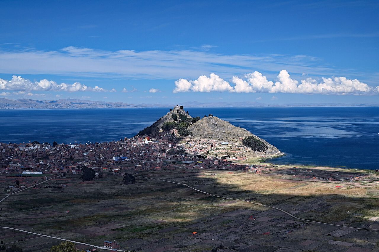 Copacabana seen from above, its low buildings spread along the Bolivian shore of Lake Titicaca beneath Cerro Calvario