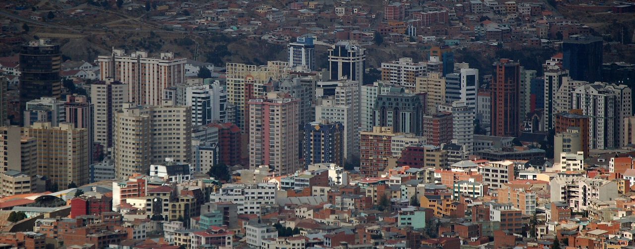Dense high-rise blocks and brick houses packed into the La Paz basin, with the bare slopes rising behind the city