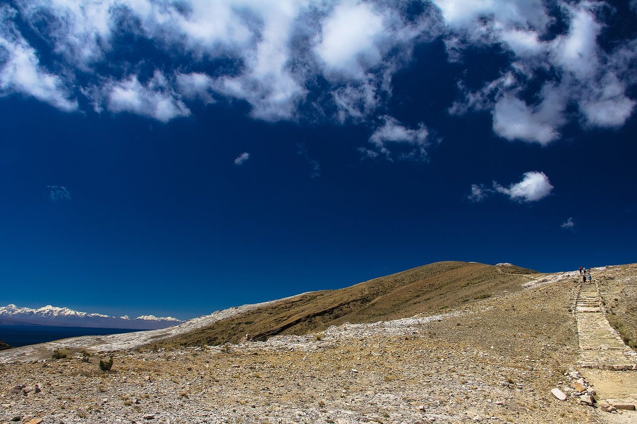 Walkers on the stone ridge path across Isla del Sol, with Lake Titicaca and the snow peaks of the Cordillera Real in the distance