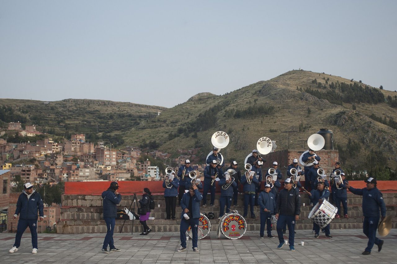 A brass band in matching blue tracksuits playing tubas, trumpets and drums on a paved terrace above Puno at first light during the Virgen de la Candelaria festival