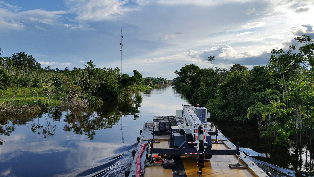 A cargo barge pushing up a narrow high-water channel lined with flooded trees on the Maranon river in the Peruvian Amazon