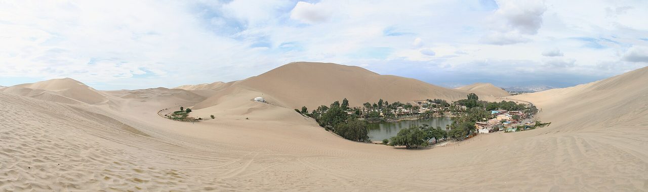The palm-fringed lagoon of Huacachina surrounded by high sand dunes in the desert outside Ica