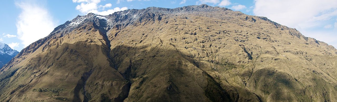 A broad grass-covered mountain flank with a small snowfield on the summit ridge in the upper Salkantay valley