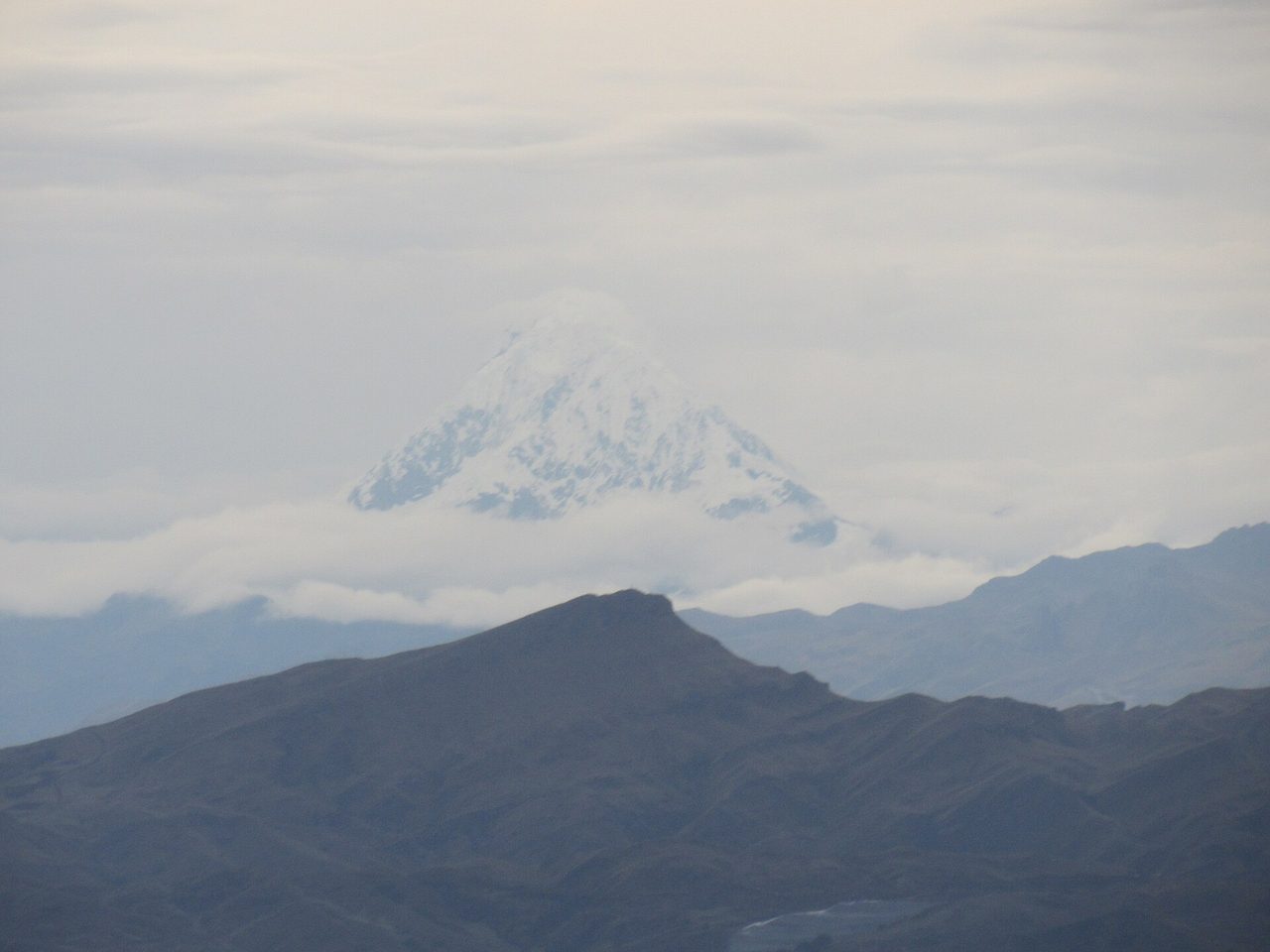 The snow-covered summit pyramid of Salkantay rising above dark ridges and a bank of cloud