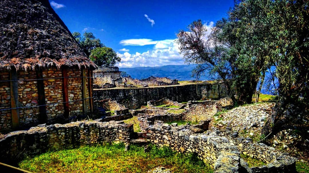 A reconstructed thatched roundhouse and circular stone house foundations inside the walls of Kuelap fortress in northern Peru