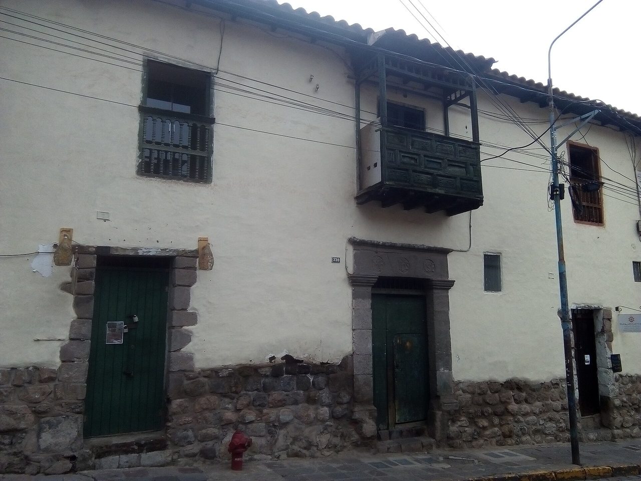 A colonial house on Calle Choquechaca in Cusco's San Blas quarter, its whitewashed upper storey and carved wooden balcony sitting on an Inca stone base