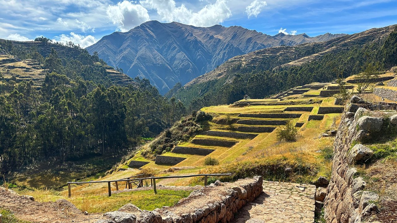 Inca agricultural terraces curving down the hillside below Chinchero, with a stone path and mountains beyond