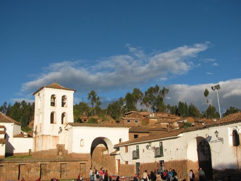 The whitewashed bell tower and arched gateway of the colonial church complex above the plaza in Chinchero