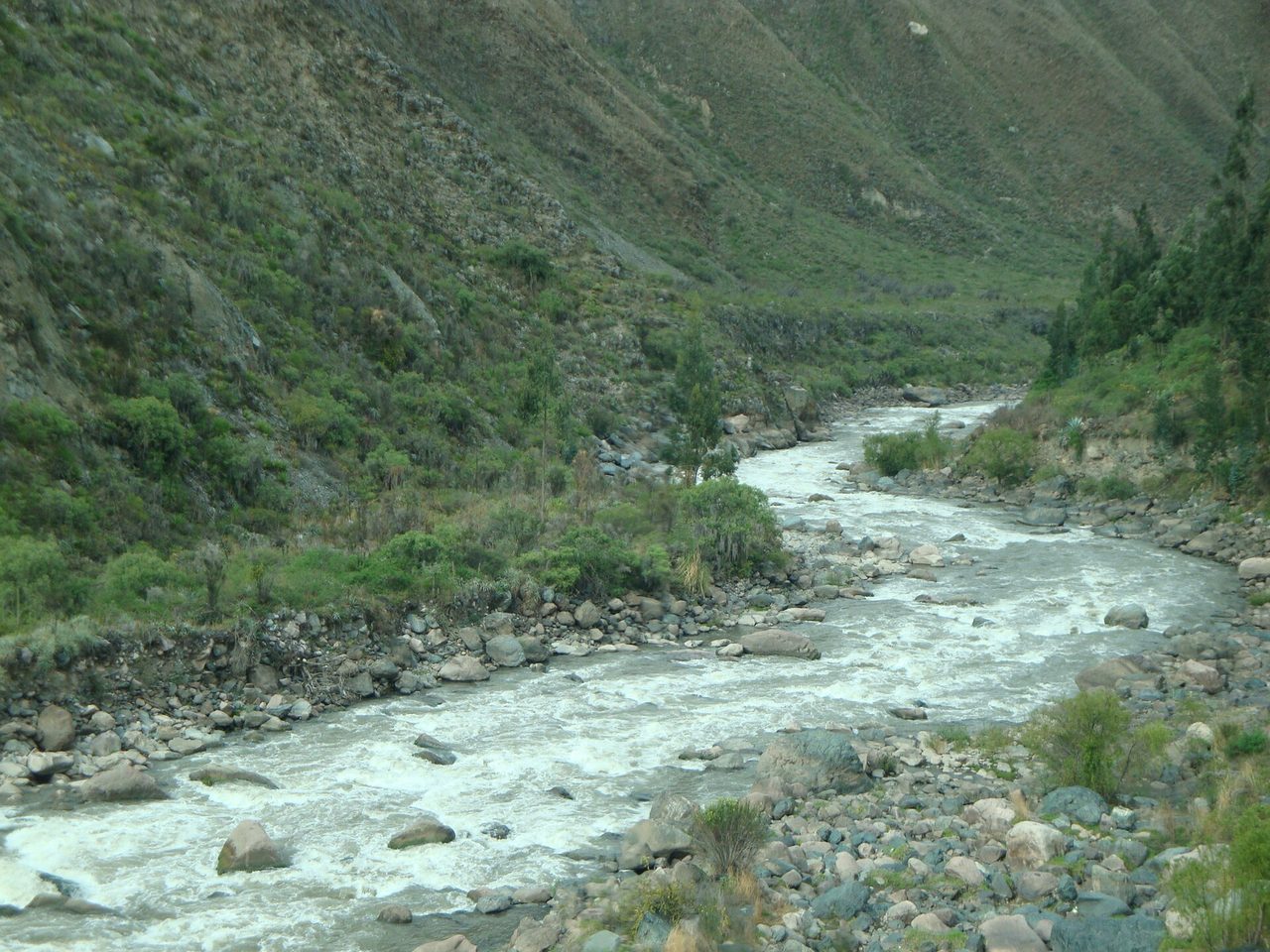 The Urubamba river running fast and shallow over boulders between steep green valley walls in the Cusco region