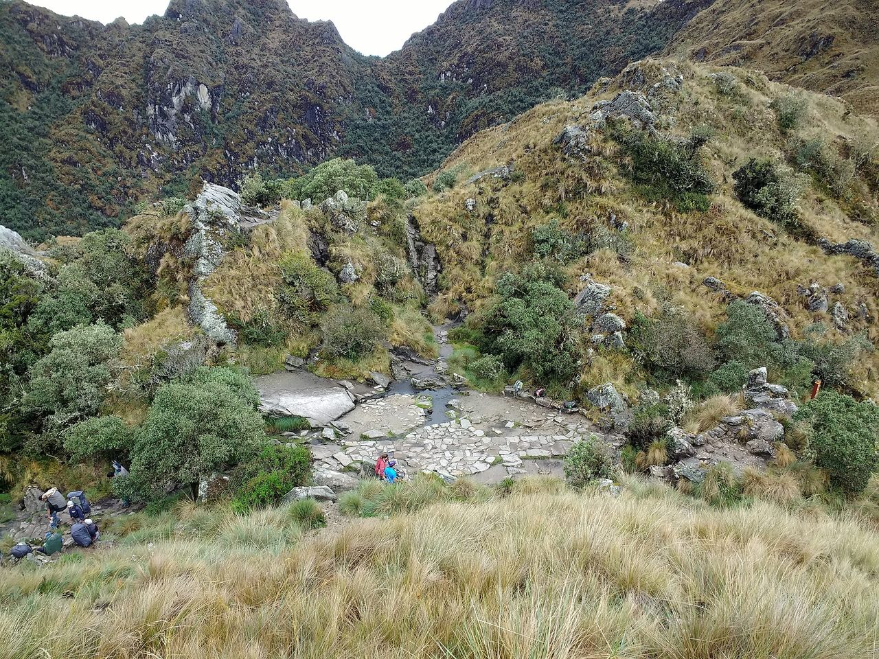 Trekkers resting beside the paved stream crossing below Runkuracay Pass on the Inca Trail