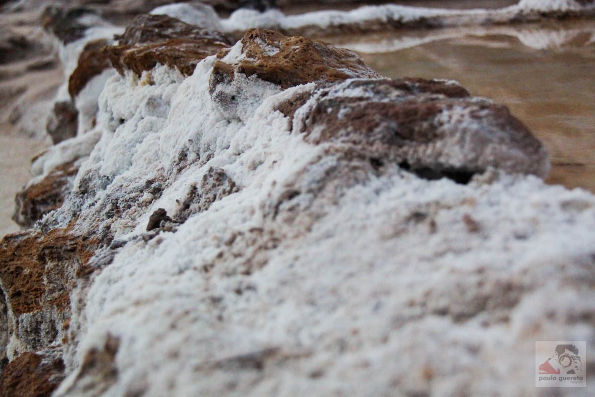 Close view of a salt-crusted earth wall dividing two evaporation pools at Maras, thick white crystals forming on the rim