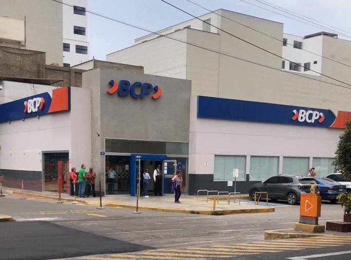 A BCP bank branch on a Lima street corner, with customers waiting outside the entrance