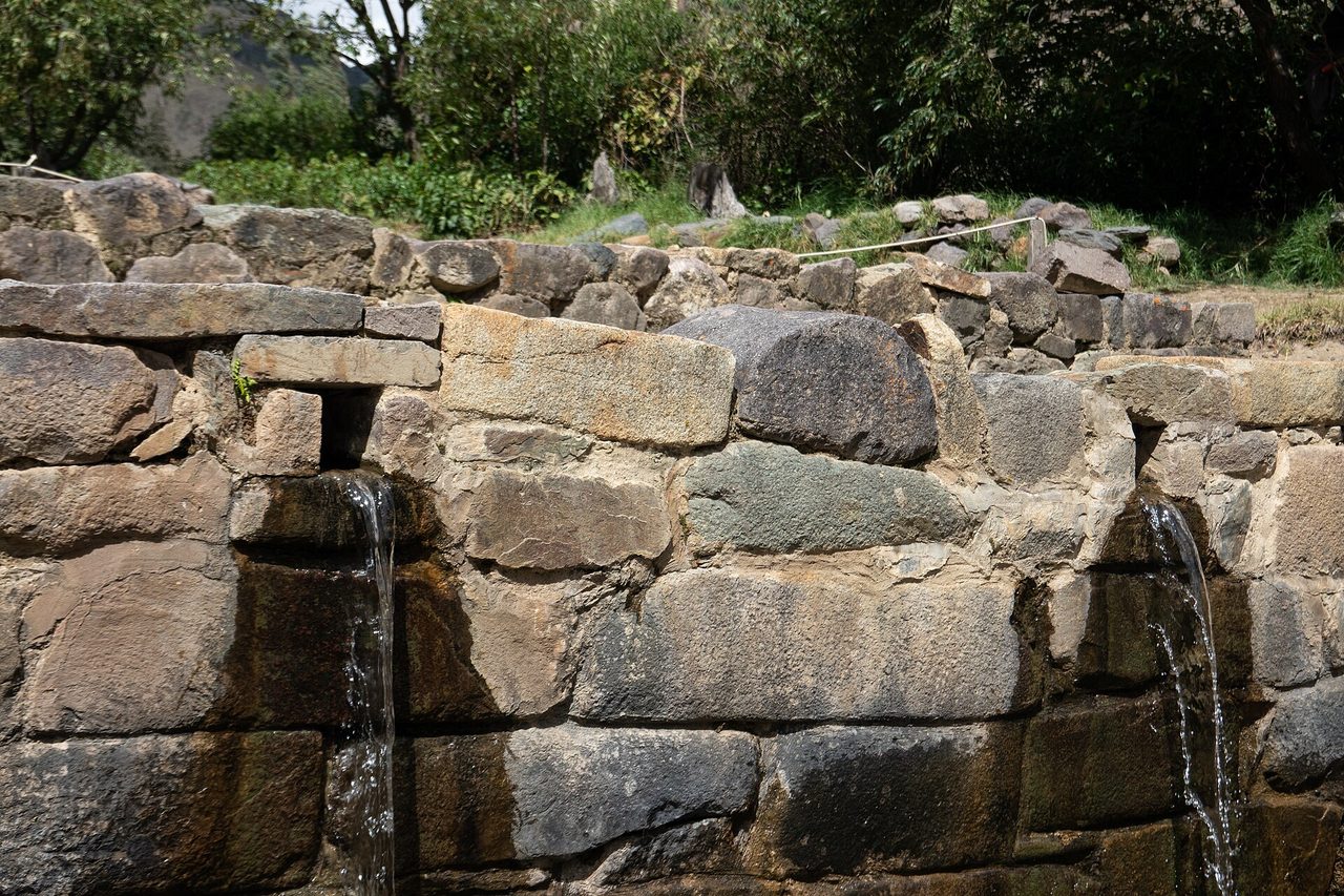 Water running from two carved stone spouts in an Inca wall at Ollantaytambo