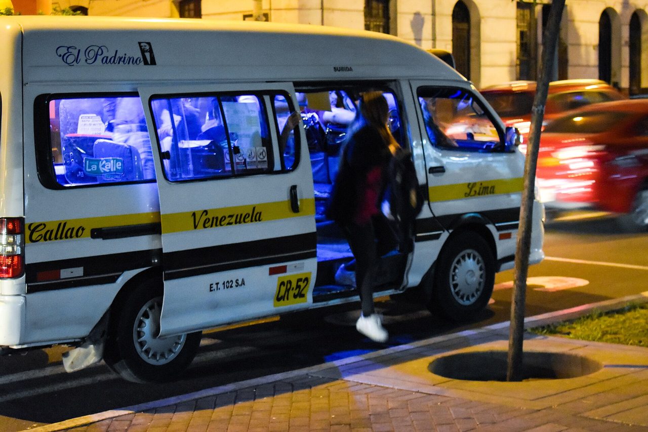 A passenger boarding a Lima combi minivan at night, its route painted along the side
