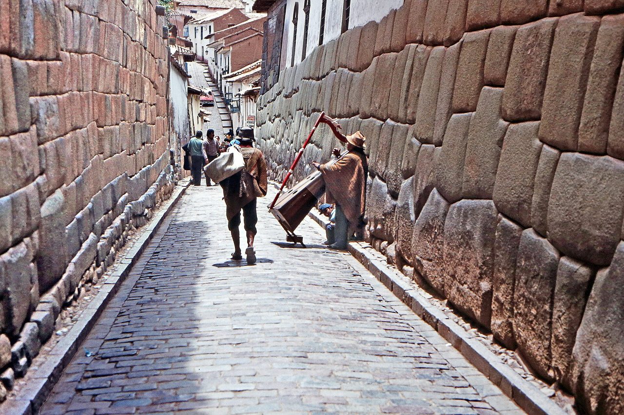 A narrow cobbled Cusco lane running between two Inca stone walls, with people walking uphill