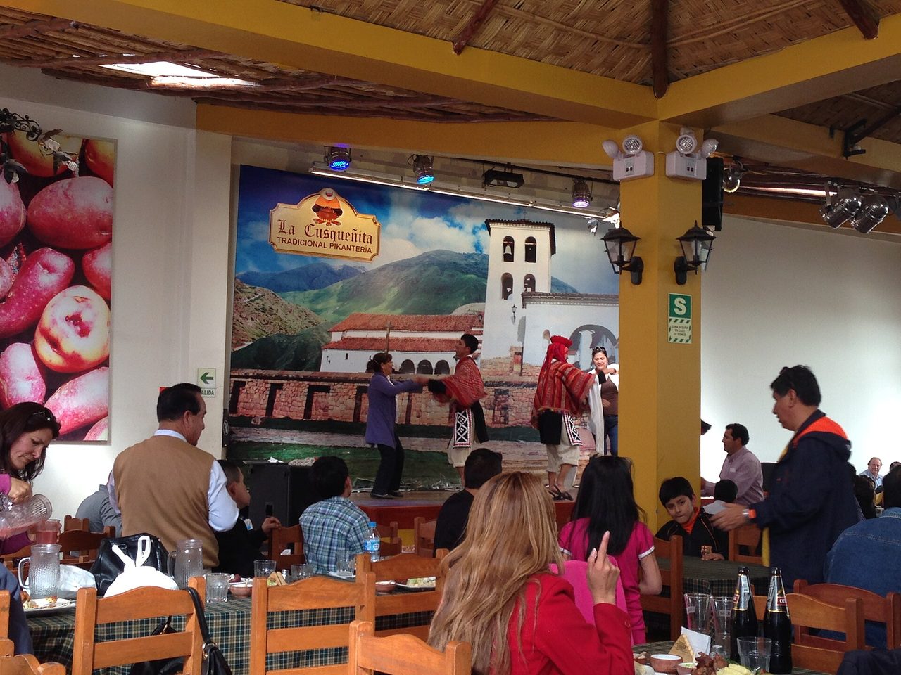 Diners at wooden tables in La Cusquenita, a busy picanteria restaurant in Cusco, watching dancers on a small stage
