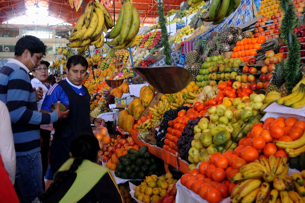 Fruit stacked high on a stall inside a covered Peruvian market hall as shoppers browse